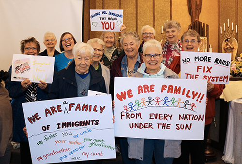 Several Franciscan Sisters of Perpetual Adoration and staff hold signs saying "We are family. From every nation under the sun." "We are family of immigrants." "No more raids! Fix the system."