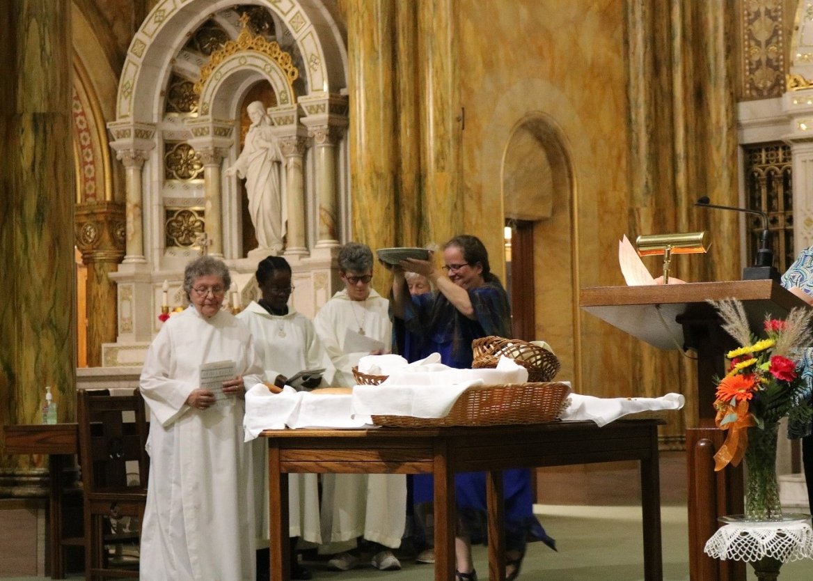 franciscan sisters dressed in white robes raise a bowl of bread for transitus