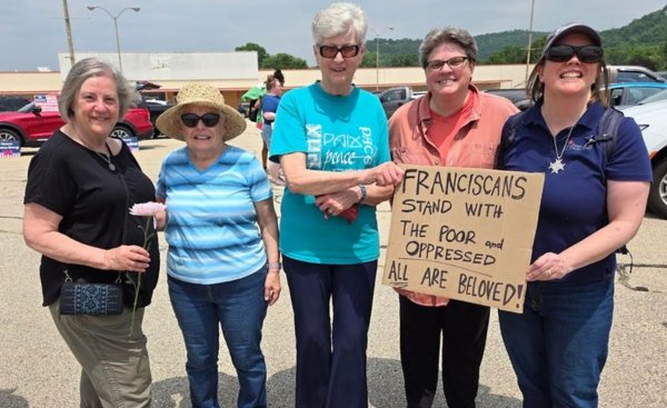 five women, four of whom are catholic sisters, attending a rally holding a sign that reads franciscans stand with the poor and oppressed, all are beloved