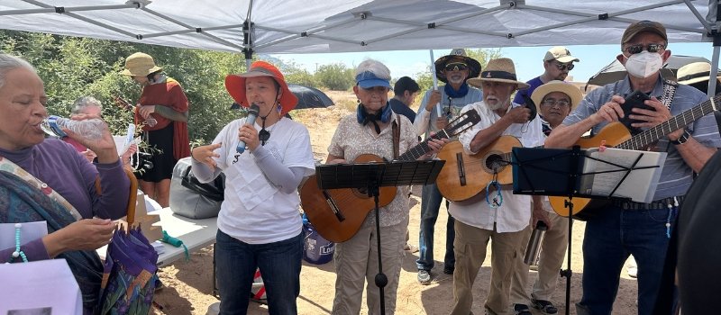 Sister Tracey Horan speaks into the microphone as musicians surround her