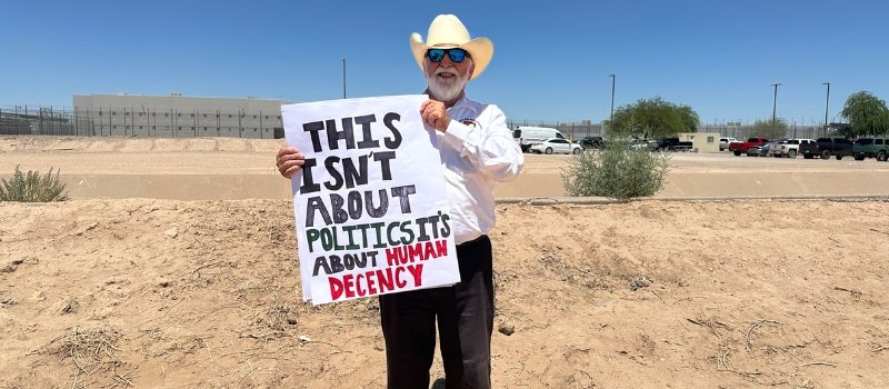 Father Pete Neeley holds a sign that reads This isn't about politics it's about human decency