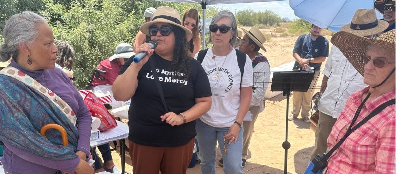 a woman is talking into a microphone as Sister Eileen McKenzie and prayer vigil attendees look on