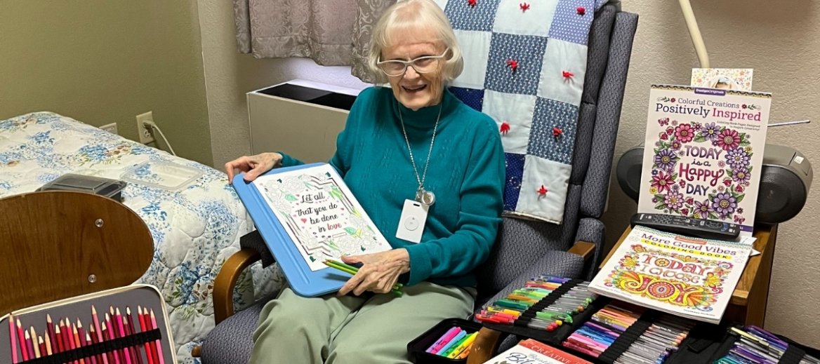 Sister Theresa Connolly is seated in a chair surrounded by pages she has colored