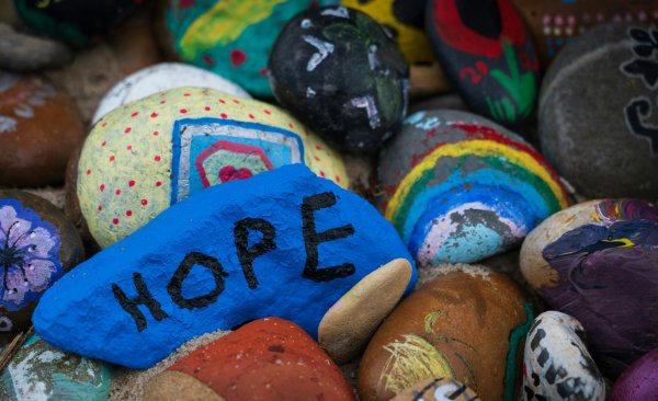 An image of a pile of small rocks painted with bright colors with a bright blue stone with the word hope painted on it in black paint.