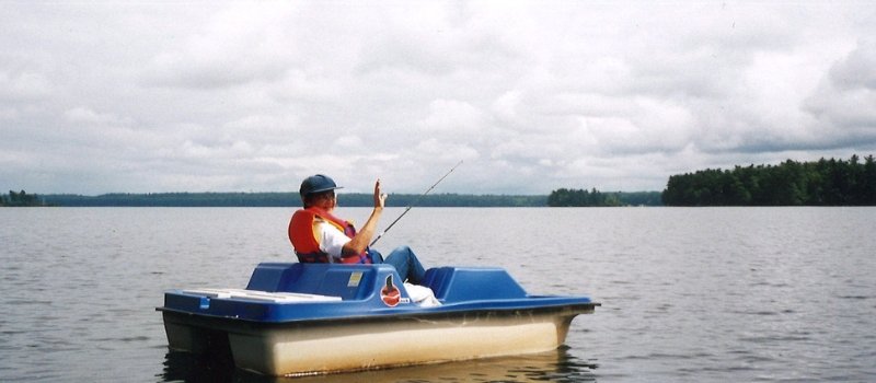 sister arlene melder wearing a life jacket and fishing off of a blue paddle boat on a lake