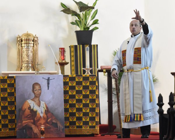 Reverend Tony Ricard raises his arm during homily for sister thea bowman celebration mass in front of painted portrait of her.