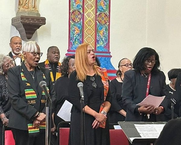 Choir of Black people dressed in black with brightly-colored suits and sashes perform at Sister Thea Bowman mass at Prince of Peace Church in Mobile, Alabama.