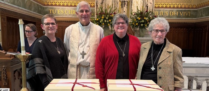 sister sue ernster, bishop joseph kopacz, sister laura nettles and sister georgia christensen pose for a photo in front of the white boxes tied with red ribbon