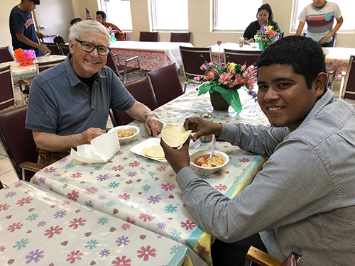 Father John Heagle eating with a refugee