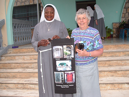 Sister Anna Nyuydini, TSSF and Sister Marla Lang, FSPA show off a banner displaying doors of congregations that formed Franciscan Common Venture and it reads "Franciscan Common Venture Opens Doors"